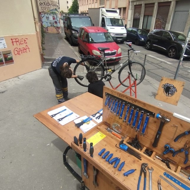 deux personnes réparant un vélo à coté de la remorque-atelier