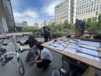 La remorque atelier-mobile est déployée. On voit des outils et deux personnes entrain de réparer un vélo