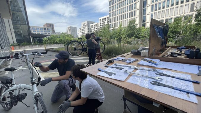 La remorque atelier-mobile est déployée. On voit des outils et deux personnes entrain de réparer un vélo